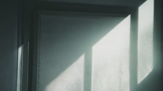 Sunlight streams onto a textured wall, creating sharp, angular shadows and highlighting the irregular surface, evoking a minimalist and peaceful atmosphere
