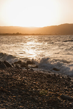 Golden sunset over the sea with waves crashing on a stony beach shore