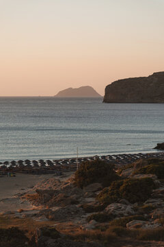 Panoramic view of rocky coastline and beach with umbrellas during golden evening.