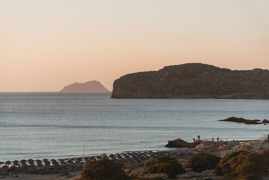 Panoramic view of rocky coastline and beach with umbrellas during golden evening.