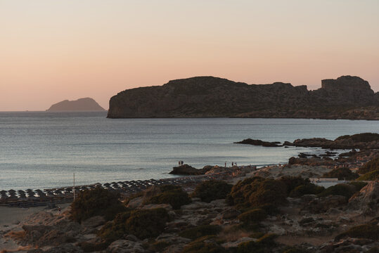 Panoramic view of rocky coastline and beach with umbrellas during golden evening.
