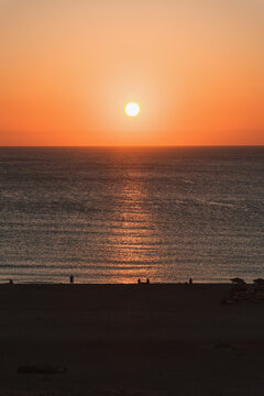 Golden sunset over the ocean with silhouettes of people on the beach at twilight.