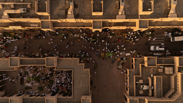 Aerial view of bustling crowds thronging Nizwa Fort's entrance, a vibrant tapestry of white against the muted ochre of ancient walls, Nizwa, Ad Dakhiliyah Governorate, Oman.