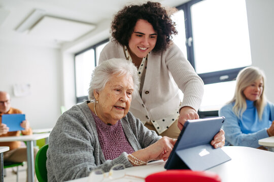 Elderly woman learning digital skills with tutor help.