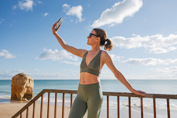 fit woman in activewear taking a selfie on a seaside balcony,