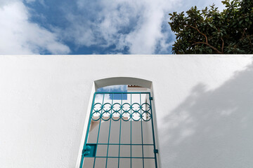 Metal gate in a white wall under blue sky in sunny courtyard architecture