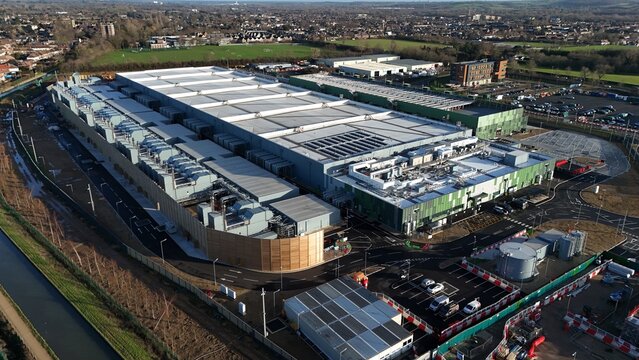 Aerial view of a sprawling data center complex with reflective rooftops and vibrant green accents amidst a network of roads, Waltham Cross, United Kingdom.