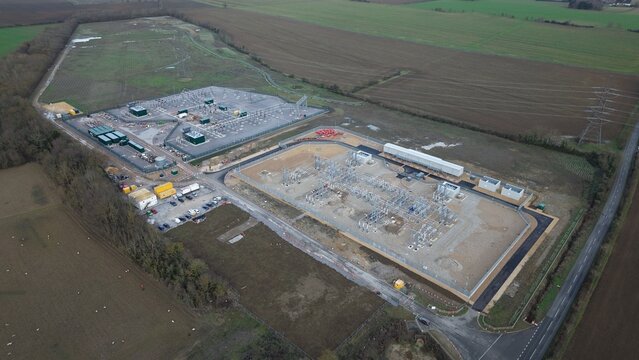 Aerial view of a sprawling substation complex, a symphony of gray infrastructure amidst the vibrant green fields, Biggleswade, United Kingdom.