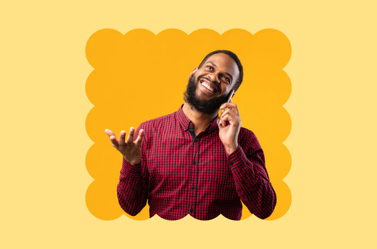 A man smiles while talking on the phone. He is standing against a bright yellow background. His expression shows enjoyment as he gestures with his free hand. This scene captures a casual moment.