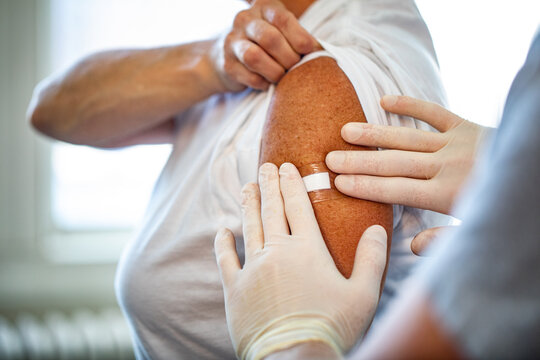 A close up of nurses hands applying a hydrocolloid bandage onto an elderly persons hand in a healthcare setting 