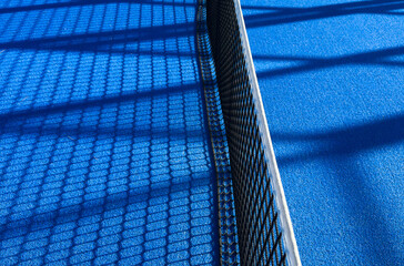 the blue synthetic grass surface of a paddle tennis court, near the net