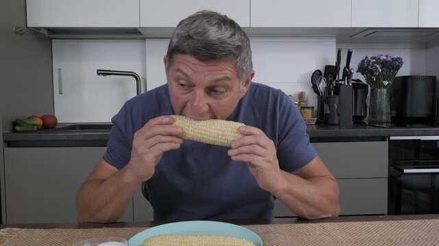 A man sits at his kitchen table, curiously examining a freshly cooked ear of corn on the cob. Sunlight streams through the window, enhancing the cheerful atmosphere.