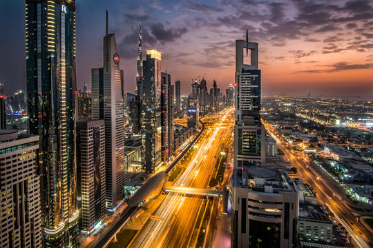 Aerial view of Sheikh Zayed Road pulsing with streaks of golden light beneath towering skyscrapers against the dusky sky, Sheik Zayed Road, Dubai, United Arab Emirates.