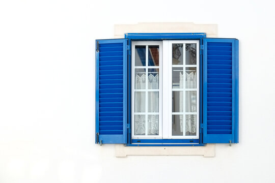 Eirceira, Portugal, Europe. This charming fishing village is a popular surf town. White home with blue shutters around a window frame. 
