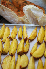Raw potato wedges seasoned with spices on baking paper sheet. Preparation of rustic country style potatoes.
