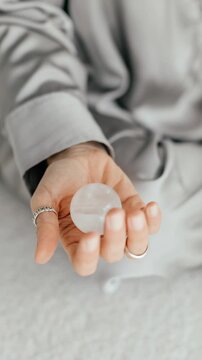 Woman dressed in a gray long-sleeve shirt holds a smooth, translucent crystal sphere in their open hand,crystal, reflecting light and highlighting its clarity.