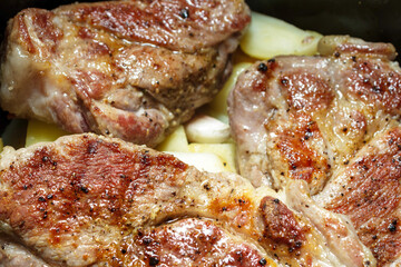 Roasted meat steaks placed on top of potatoes in a pan. Cooking hearty homemade dinner dish.
