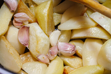 Raw potato chunks mixed with unpeeled garlic cloves in a pan. Preparation of roasted vegetable dish.