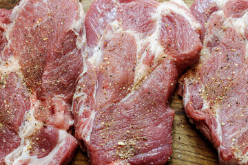 Close up texture of raw pork neck steaks seasoned with spices and pepper. Uncooked red meat background.