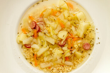 Top view of vegetable cabbage soup or kapusniak in a white bowl. Traditional homemade hot liquid dish.