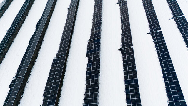 Aerial view of rows of solar panels stand stark against the pristine white snow, creating a geometric contrast of sustainable energy, Sremska Mitrovica, Vojvodina, Serbia.