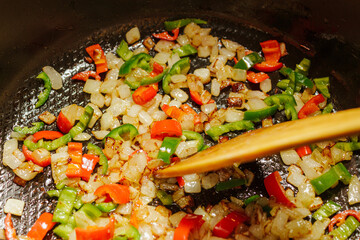 Frying chopped onions and peppers in a pan with a wooden spoon. Cooking vegetable saute process close up.