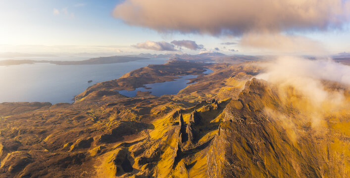 Aerial view of golden light caresses the craggy peaks and glassy lochs, while wisps of cloud dance across the rugged landscape, Portree, Scotland, United Kingdom.