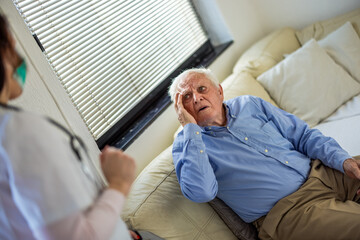 Fototapeta premium Nurse talking to senior man on sofa at home in the living room while he explains his health concerns