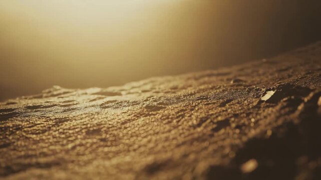 Dark rough textured surface creating an abstract landscape, illuminated by a warm, soft golden light, providing a mysterious and dramatic cosmic aesthetic