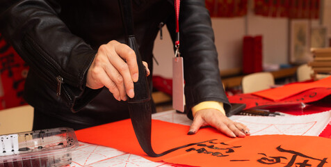 Close up of woman writing Happy New Year with Chinese calligraphy on couplets for celebration. Chinese calligraphy workshop - create traditional festive symbols and Chinese characters