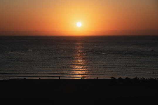 Golden sunset over the calm sea with silhouettes of people on beach.