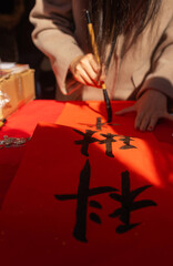 Close up of woman writing Happy New Year with Chinese calligraphy on couplets for celebration. Chinese calligraphy workshop - create traditional festive symbols and Chinese characters