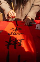 Close up of woman writing Happy New Year with Chinese calligraphy on couplets for celebration. Chinese calligraphy workshop - create traditional festive symbols and Chinese characters