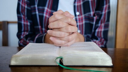 Person with clasped hands praying over an open bible, seeking spiritual guidance, reflecting on faith, devotion, and religious study