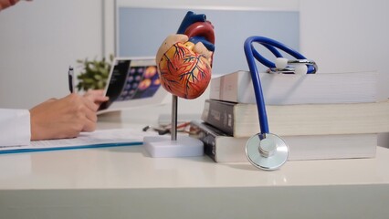 Doctor studying human heart anatomy model, reviewing medical records for cardiology diagnosis and...