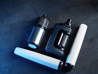 Electronic cigarettes on a dark wooden table. Disposable electronic cigarettes and a device with a replaceable vaporizer and liquid