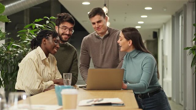 Diverse creative team collaborating around laptop in modern office