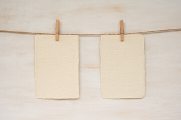 Two sheets of handmade paper hanging from a rope against a wooden background