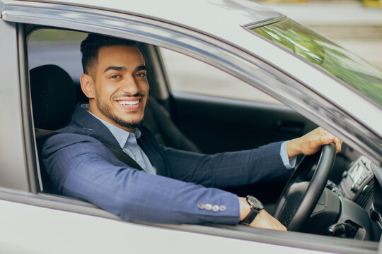 Photo of wealthy middle-eastern businessman in stylish suit driving nice car, going to office, having important business meeting, looking through window and smiling at camera, side view.