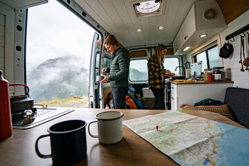 Obraz premium Two people prepare drinks inside a camper van with a scenic foggy mountain view outside the open door. Concept of adventure, travel, camping, and outdoor lifestyle.