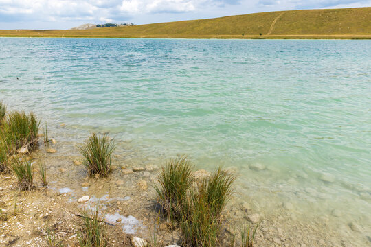 A tranquil turquoise lake lapping a rocky, pebbled shore