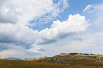 Obraz premium Dramatic clouds drift over rolling hills and a wide meadow