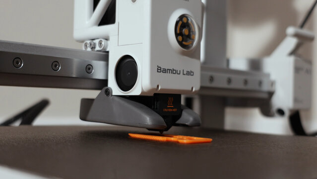 Close-up of a 3D printer nozzle depositing molten plastic onto an orange object