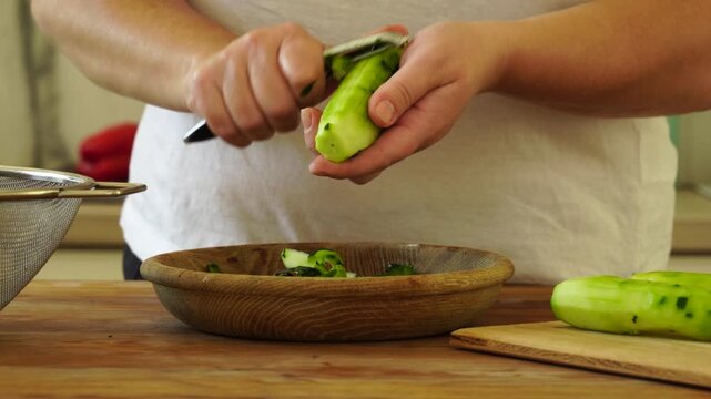 Woman cutting fresh cucumber for salad

