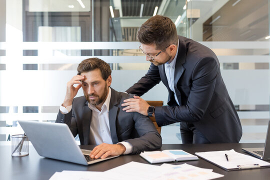Business professional experiencing stress and receiving empathetic support from a colleague, finding resolution and help in a challenging office environment while working on a laptop