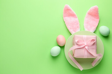 Painted Easter eggs, bunny ears headband and gift on green background, flat lay. Space for text