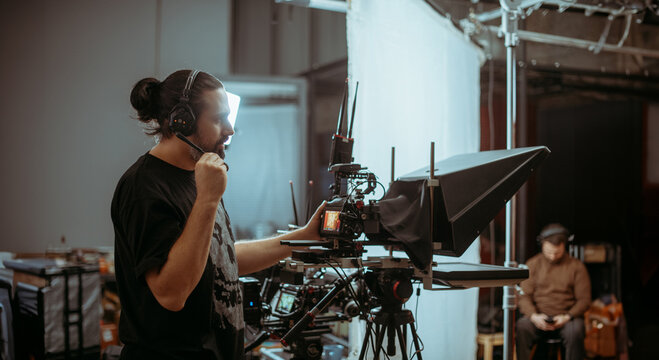 Director of photography with a camera in his hands on the set. Professional videographer at work on filming a movie, commercial or TV series. Filming process indoors, studio