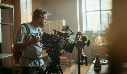 Fototapeta na wymiar Director of photography with a camera in his hands on the set. Professional videographer at work on filming a movie, commercial or TV series. Filming process indoors, studio