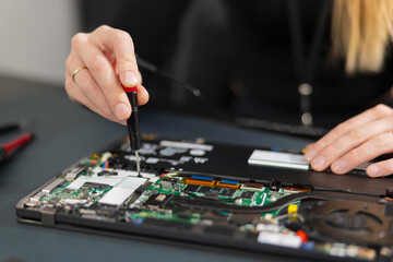 Female IT technician repairs a laptop internals with a screwdriver on a workbench during hardware...
