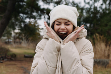 Winter scene with a joyful woman wearing a thick coat and beanie, smiling with hands near her face,...